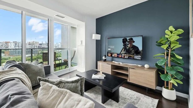 Uma sala de estar moderna com uma televisão grande, um sofá, uma mesa de centro e um vaso com planta.