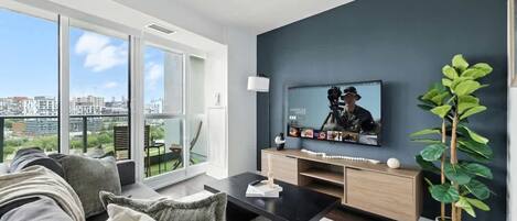 Ein modernes Wohnzimmer mit großem Fernseher, einer Couch, einem Couchtisch und einer Topfpflanze.
