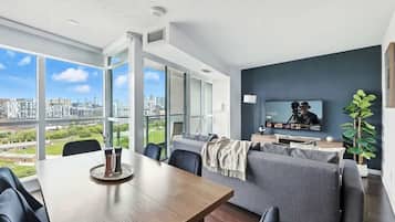 A modern living room with a dining area, large windows, and a city view.