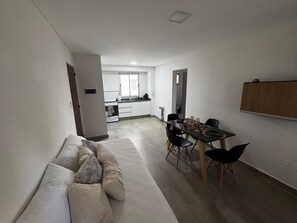 A modern living room with a sofa, dining table, and chairs. A kitchen is visible in the background. - Modern, comfortable apartment in Salta with an excellent location — VRTEAM (Salta)