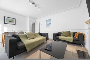 A modern living room with two sofas, a coffee table, and a dining area with chairs and a table. - City Centre 3 bed flat with lift and roof terrace (Greater London)