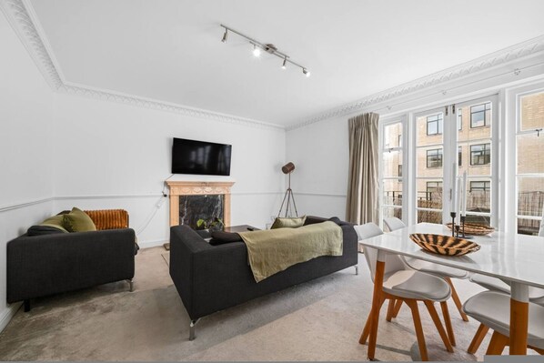 A modern living room with a fireplace, a television, and a dining area with a view of the city. - City Centre 3 bed flat with lift and roof terrace (Greater London)