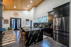 A modern kitchen with a black marble island, stainless steel appliances, and a wooden ceiling. - Sauna, Hot Tub, Fire Pit, Pets, EV Plug, Secluded (Broken Bow)