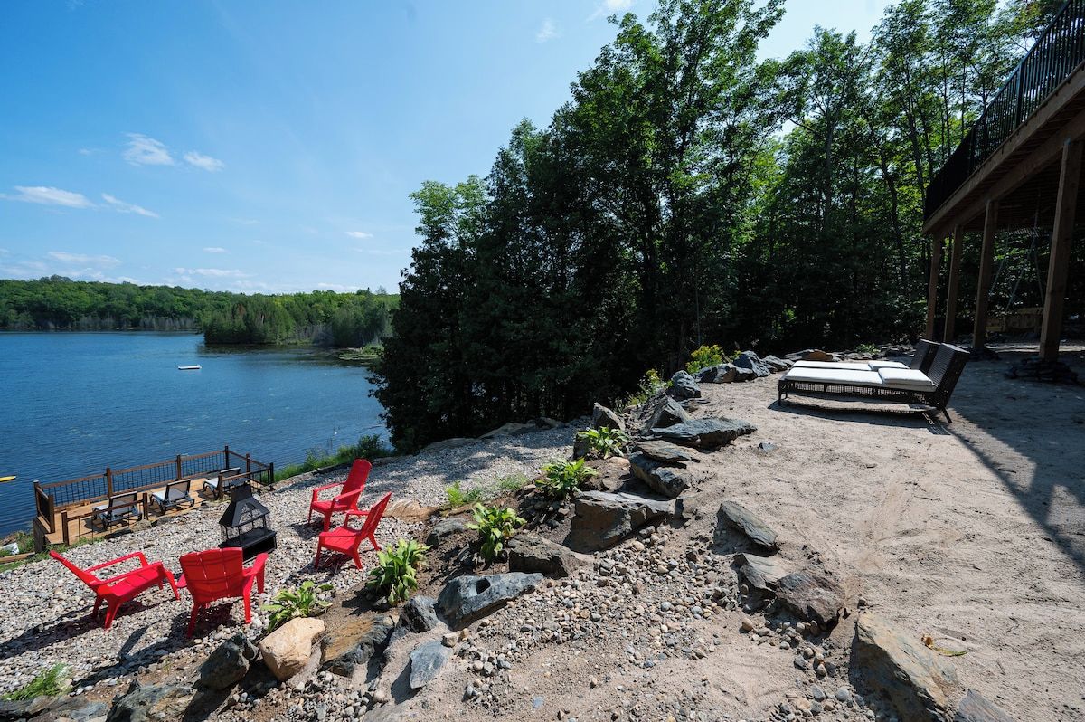 A lakeside deck with red chairs, a grill, and a covered seating area.
