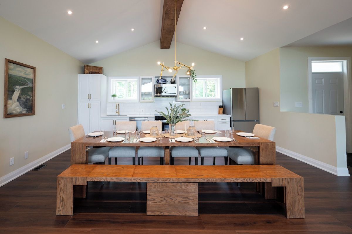 A dining area with a wooden table set for six, white cabinets, and a hanging light fixture.