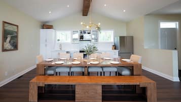 A dining area with a wooden table set for six, white cabinets, and a hanging light fixture.