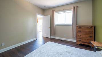 A bedroom with a large bed, a dresser, a window with curtains, and a door leading to another room.
