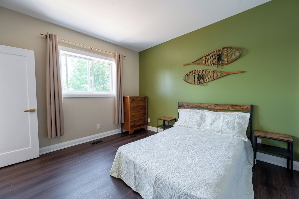 A bedroom with a bed, a dresser, a window with curtains, and two wall-mounted decorative items.