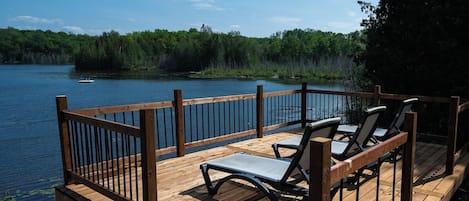 Une terrasse en bois dotée d’une rambarde, qui offre une vue sur un lac, et aménagée avec des chaises longues.