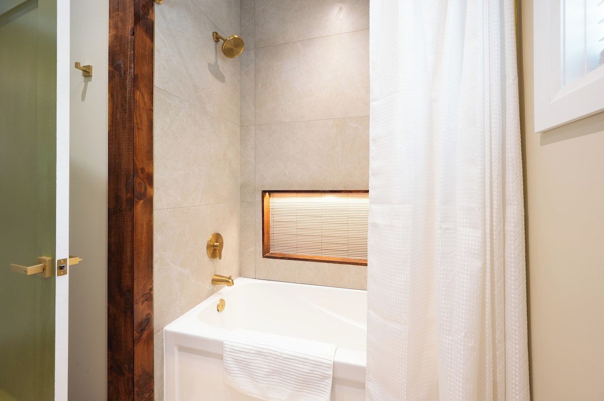 A bathroom with a bathtub, a showerhead, and a window with blinds.