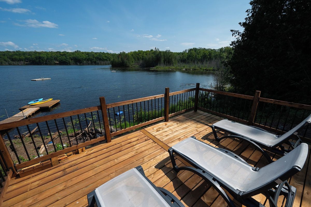 A wooden deck with lounge chairs overlooking a lake.