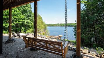 Un banco de madera para columpios bajo un porche con vista a un lago y bosque.