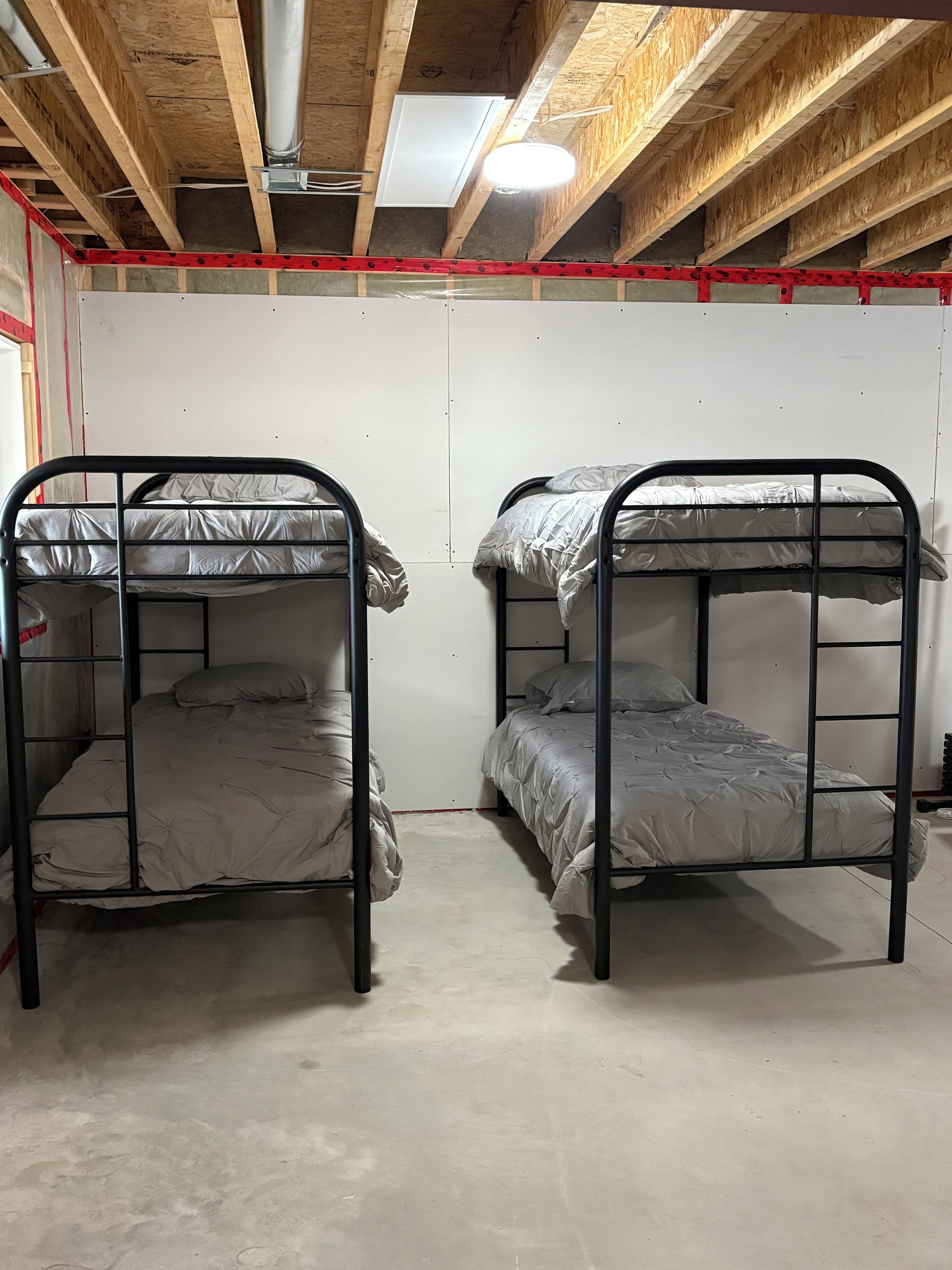 A room with two bunk beds, wooden ceiling beams, and a white wall.
