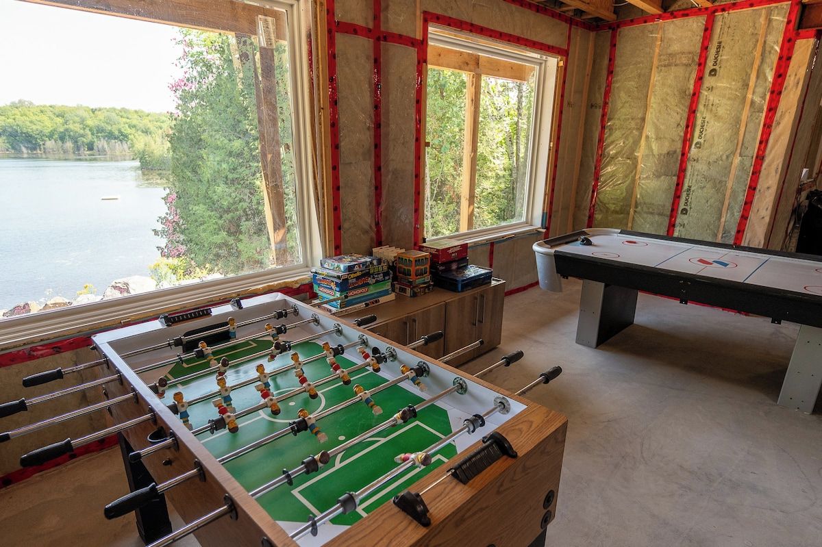 Ett rum med ett fotbollsspel, ett biljardbord och ett fönster med utsikt över en sjö.