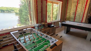 Ett rum med ett fotbollsspel, ett biljardbord och ett fönster med utsikt över en sjö.