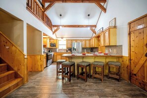 Eine Küche mit Holzausstattung, einer zentralen Kochinsel inklusive Sitzgelegenheiten und einer Treppe mit Holzhandläufen.