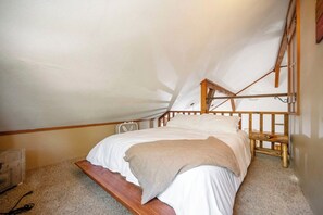 Ein Schlafzimmer mit einem hölzernen Bett, einer schrägen Decke und einem kleinen Fenster.