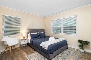 A bedroom with a bed, bedside table, lamp, chair, and a potted plant.