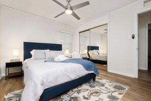 Een slaapkamer met een bed, nachtkastje, spiegel en plafondventilator.