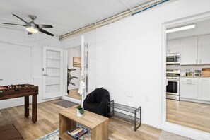 A modern living room with a foosball table, a coffee table with books, a black chair, and a ceiling fan.