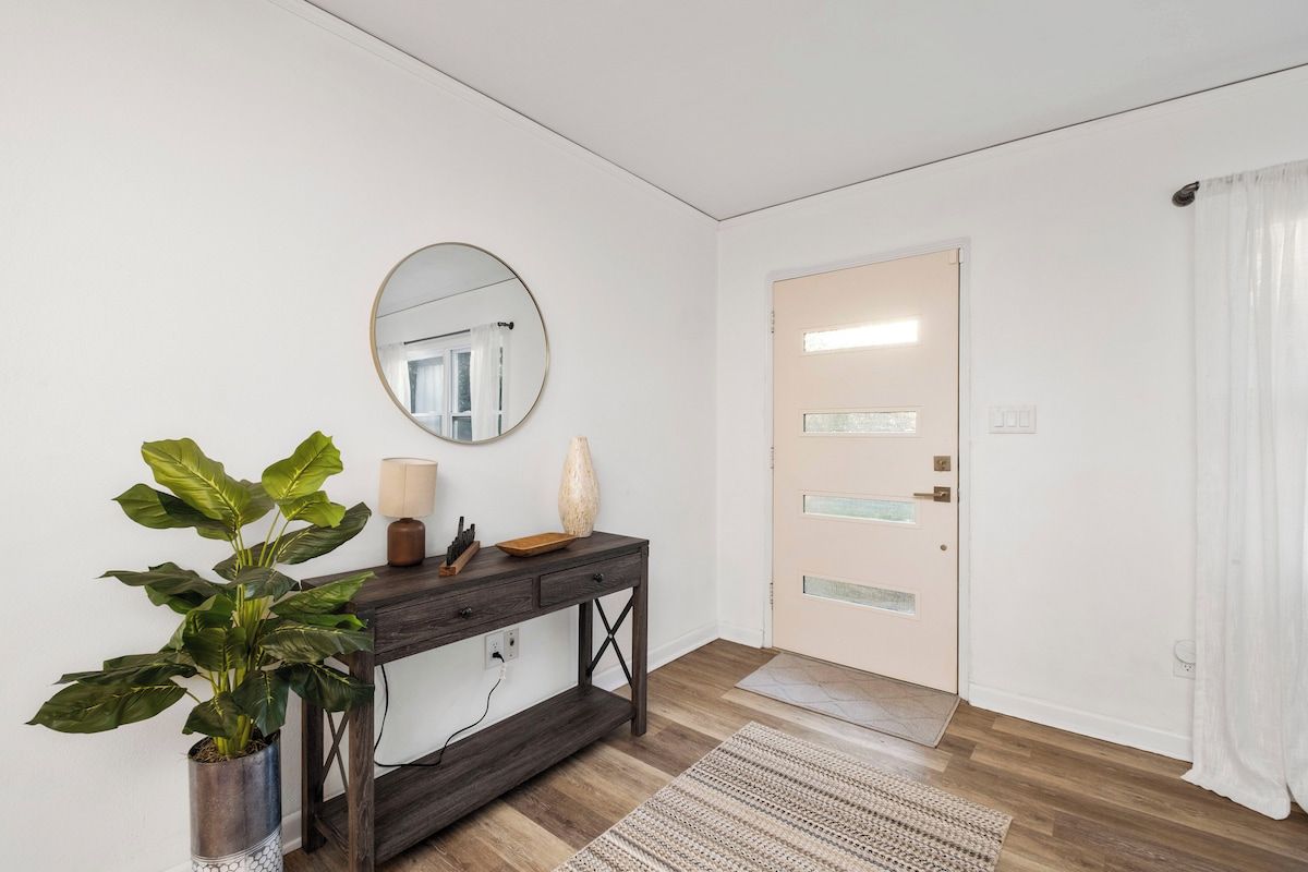 Quarto com uma mesa consola de madeira, planta em vaso, espelho e porta com painéis de vidro jateado.