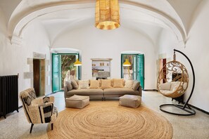 A spacious living room with a high arched ceiling, a brown sofa with cushions, a round woven rug, a hanging chair, and a radiator.