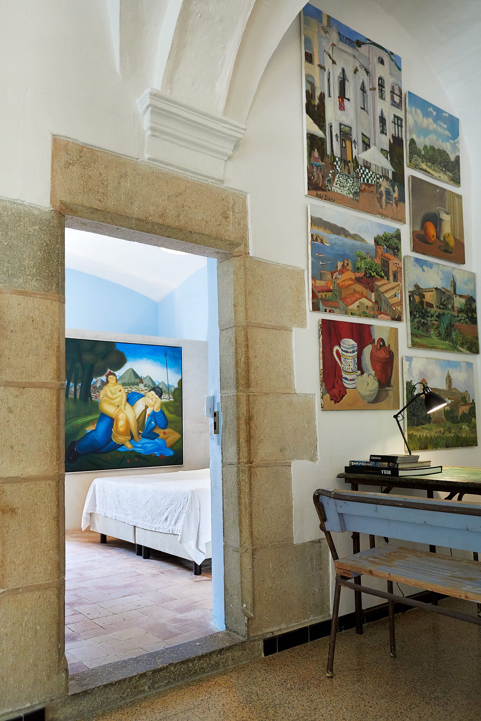 A room with a bed, a desk, and various paintings on the wall.