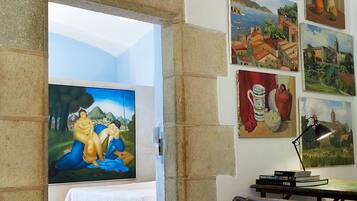 A room with a bed, a desk, and various paintings on the wall.