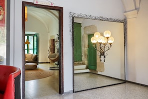 Une pièce avec un grand miroir qui reflète une porte verte, un fauteuil en osier et un lampadaire.