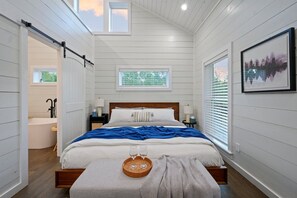 A bedroom with a bed, a bedside table, a nightstand, a window, and a door leading to a bathroom. - Under the Stars: Secluded, Hot Tub, Firepit, Pets (Broken Bow)