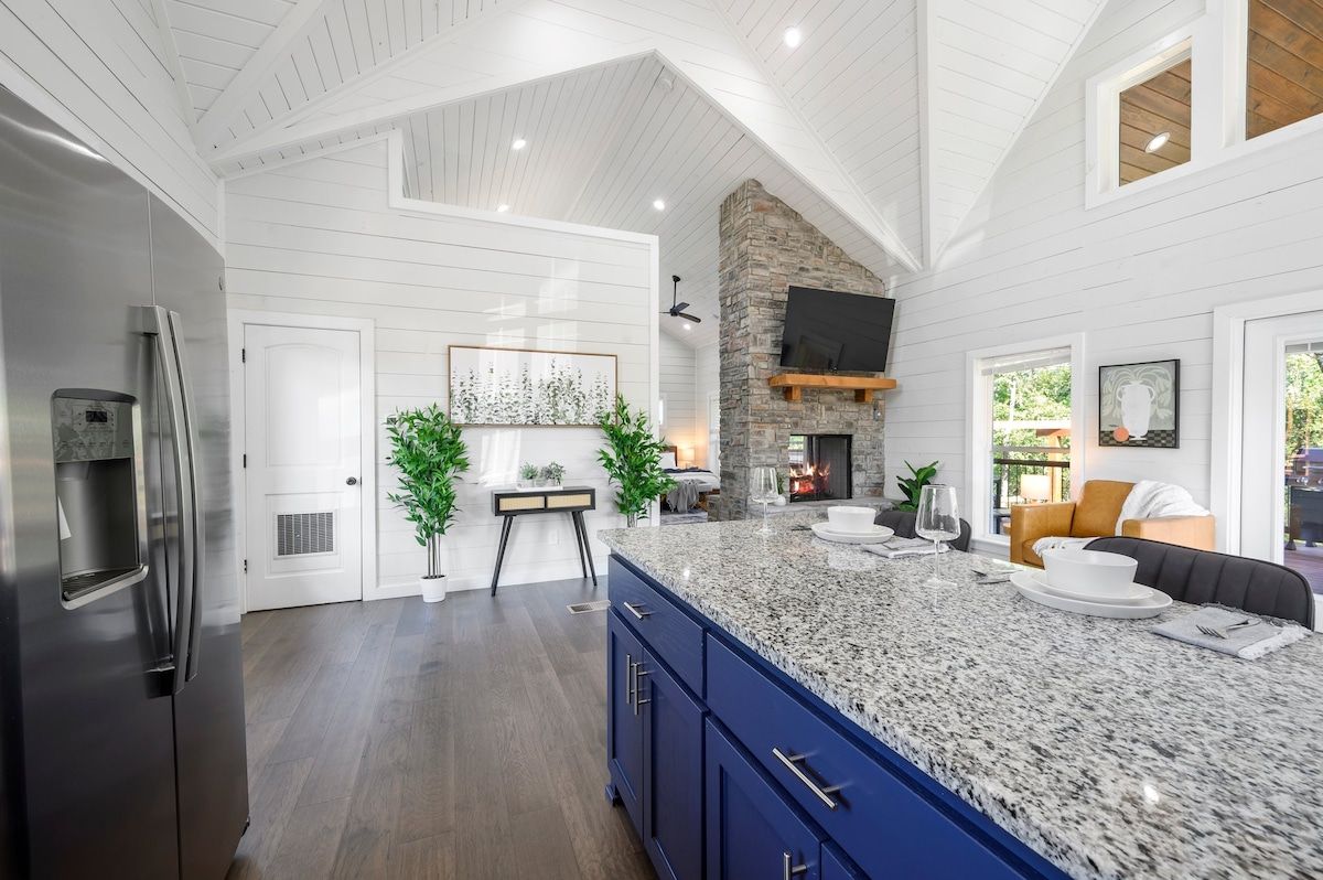 A spacious kitchen with a large island, a stone fireplace, and a modern stainless steel refrigerator.