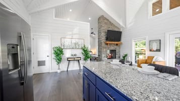 A spacious kitchen with a large island, a stone fireplace, and a modern stainless steel refrigerator.