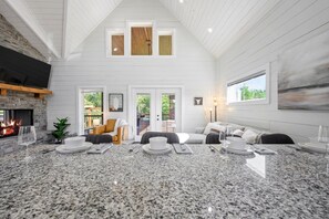 A spacious living area with a high ceiling, a fireplace, a dining table set for four, and a comfortable seating arrangement. - Under the Stars: Secluded, Hot Tub, Firepit, Pets (Broken Bow)