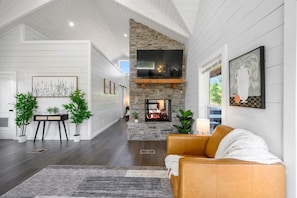 A spacious living room with a stone fireplace, a large flat-screen TV mounted above it, and a comfortable leather sofa. - Under the Stars: Secluded, Hot Tub, Firepit, Pets (Broken Bow)
