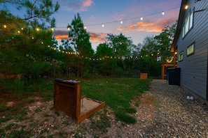 A backyard with a wooden bench, string lights, and a house. - Under the Stars: Secluded, Hot Tub, Firepit, Pets (Broken Bow)