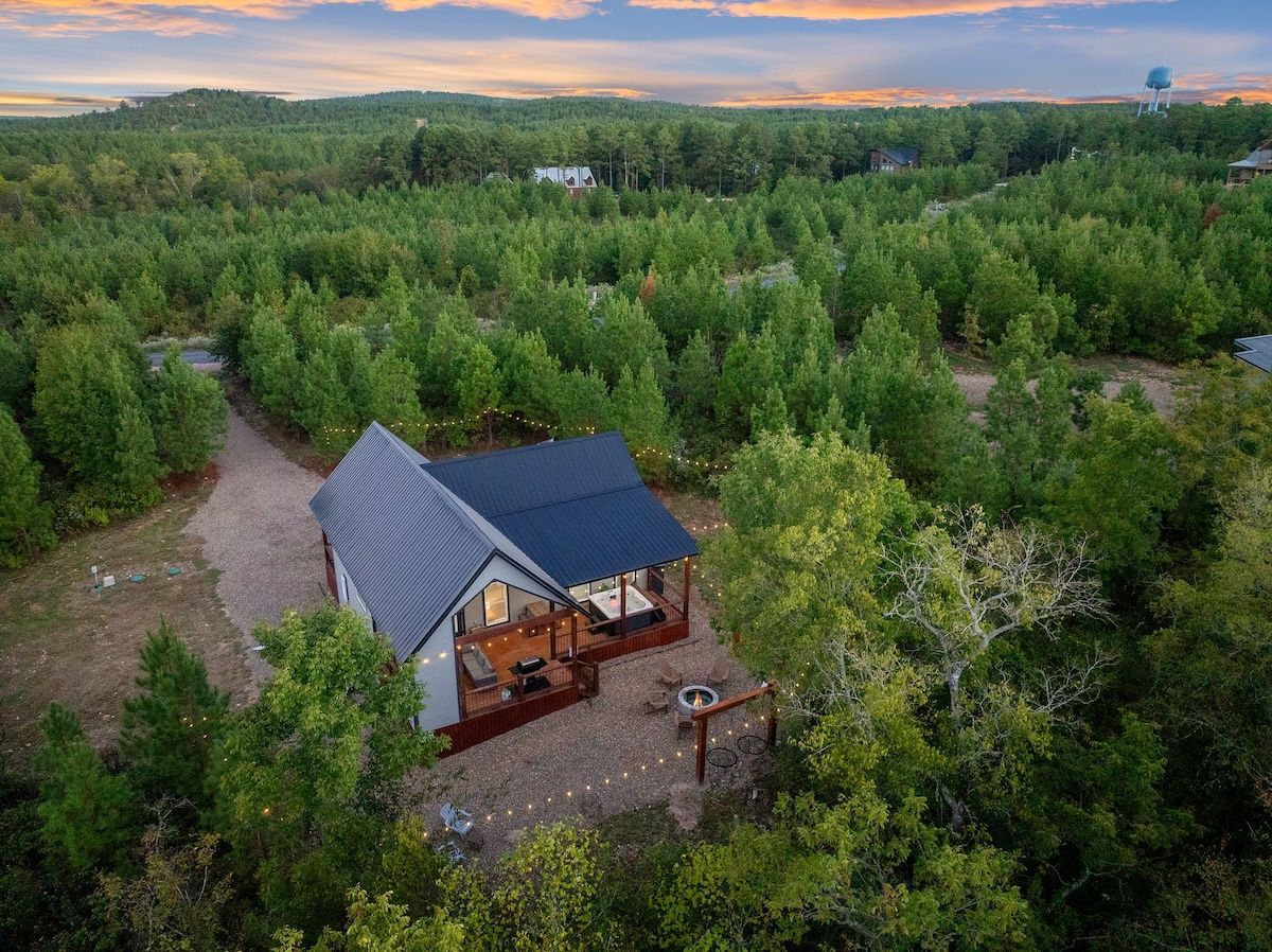 A cabin with a deck, surrounded by dense forest, with a clear view of the sky.