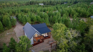 A cabin with a deck, surrounded by dense forest, with a clear view of the sky.