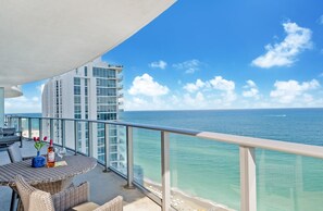 Ein Balkon mit Meerblick, ein Esstisch mit Stühlen und eine Weinflasche.