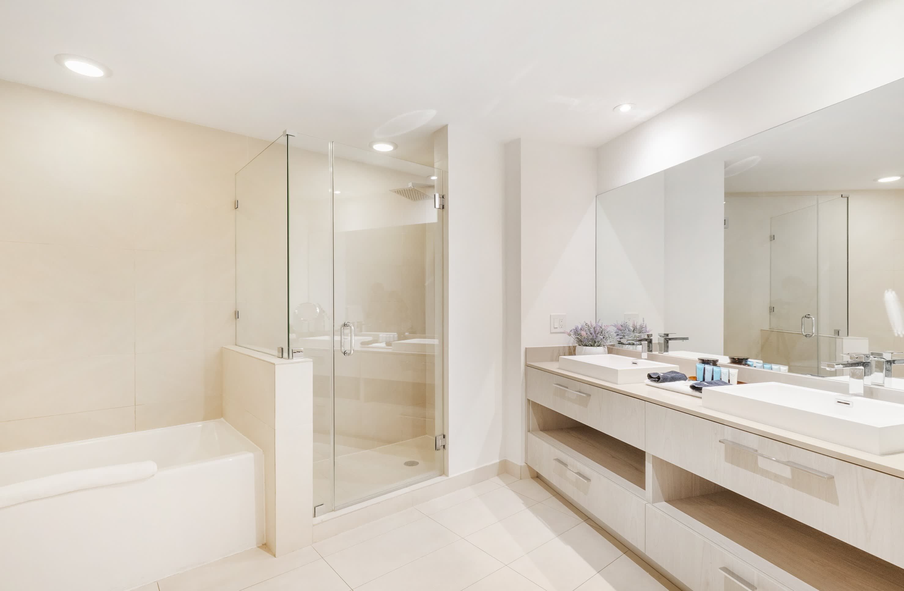 A modern bathroom with a glass-enclosed shower, a large mirror, and a vanity with two sinks.