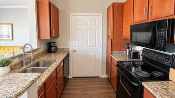 A kitchen with wooden cabinets, a black stove, a microwave, and granite countertops.