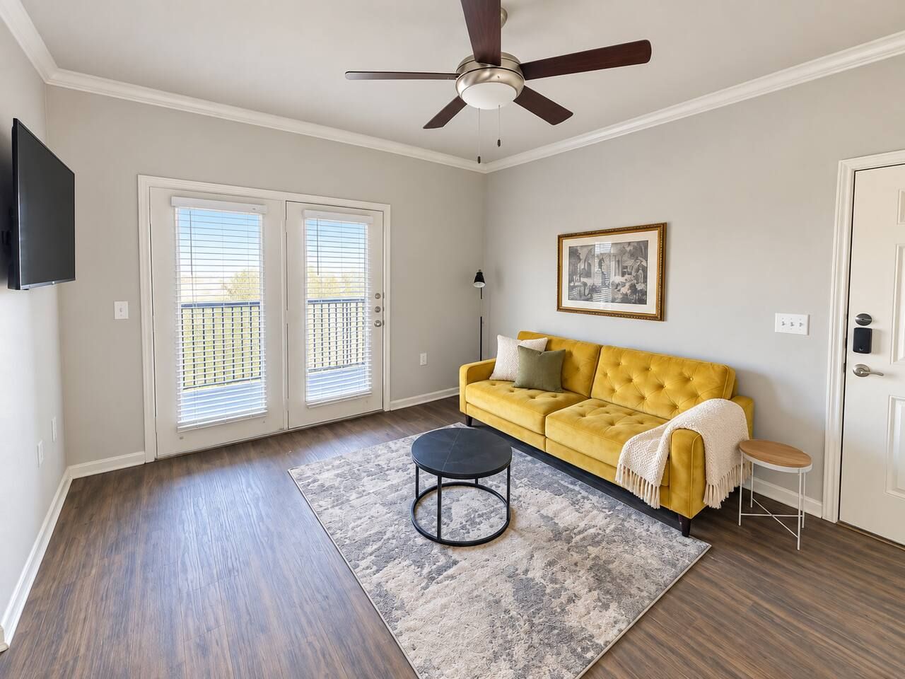 A living room with a yellow sofa, a round coffee table, a ceiling fan, and a door with a window.
