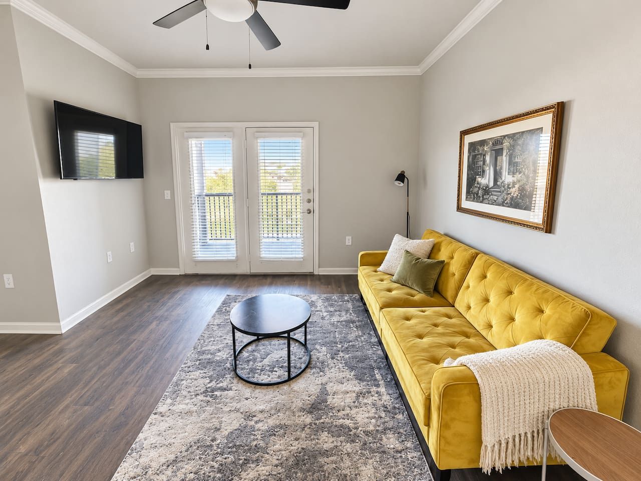 A living room with a yellow sofa, a round coffee table, and a ceiling fan.