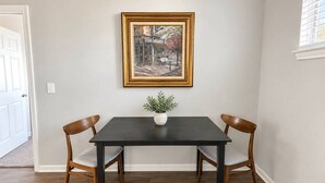 Una mesa de comedor con dos sillas, un cuadro enmarcado encima y una planta pequeña sobre la mesa.