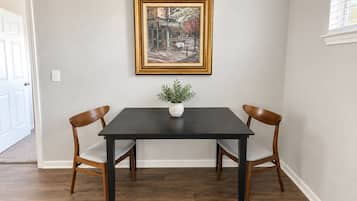 A dining table with two chairs, a framed painting above it, and a small plant on the table.