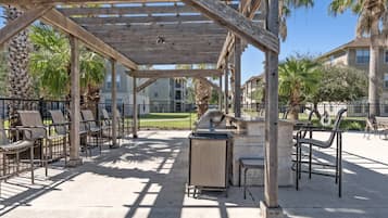 An outdoor patio area with a pergola, seating, and a barbecue grill.