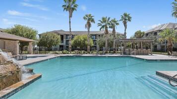 A swimming pool with a waterfall feature, surrounded by palm trees and a covered seating area.