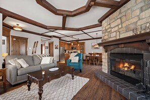 A spacious living room with a fireplace, wooden beams, stone wall, and a cozy seating area. - The Sanctuary at Les Manoirs (Mont Tremblant)