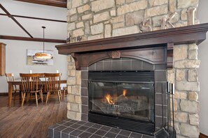A stone fireplace with a glass door, a wooden mantel, and a dining area with chairs and a table. - The Sanctuary at Les Manoirs (Mont Tremblant)