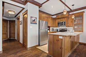 A kitchen with wooden cabinets, a stainless steel refrigerator, a microwave, and pendant lights. - The Sanctuary at Les Manoirs (Mont Tremblant)