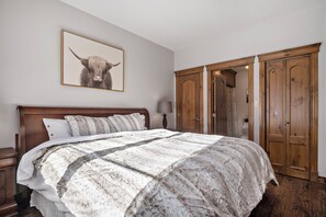 A bedroom with a large bed, a wooden wardrobe, and a framed picture on the wall. - The Sanctuary at Les Manoirs (Mont Tremblant)